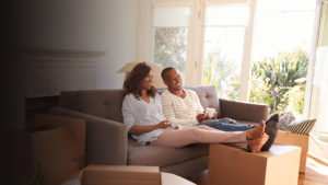 Family sitting on couch in new home relaxing between moving and unpacking boxes.